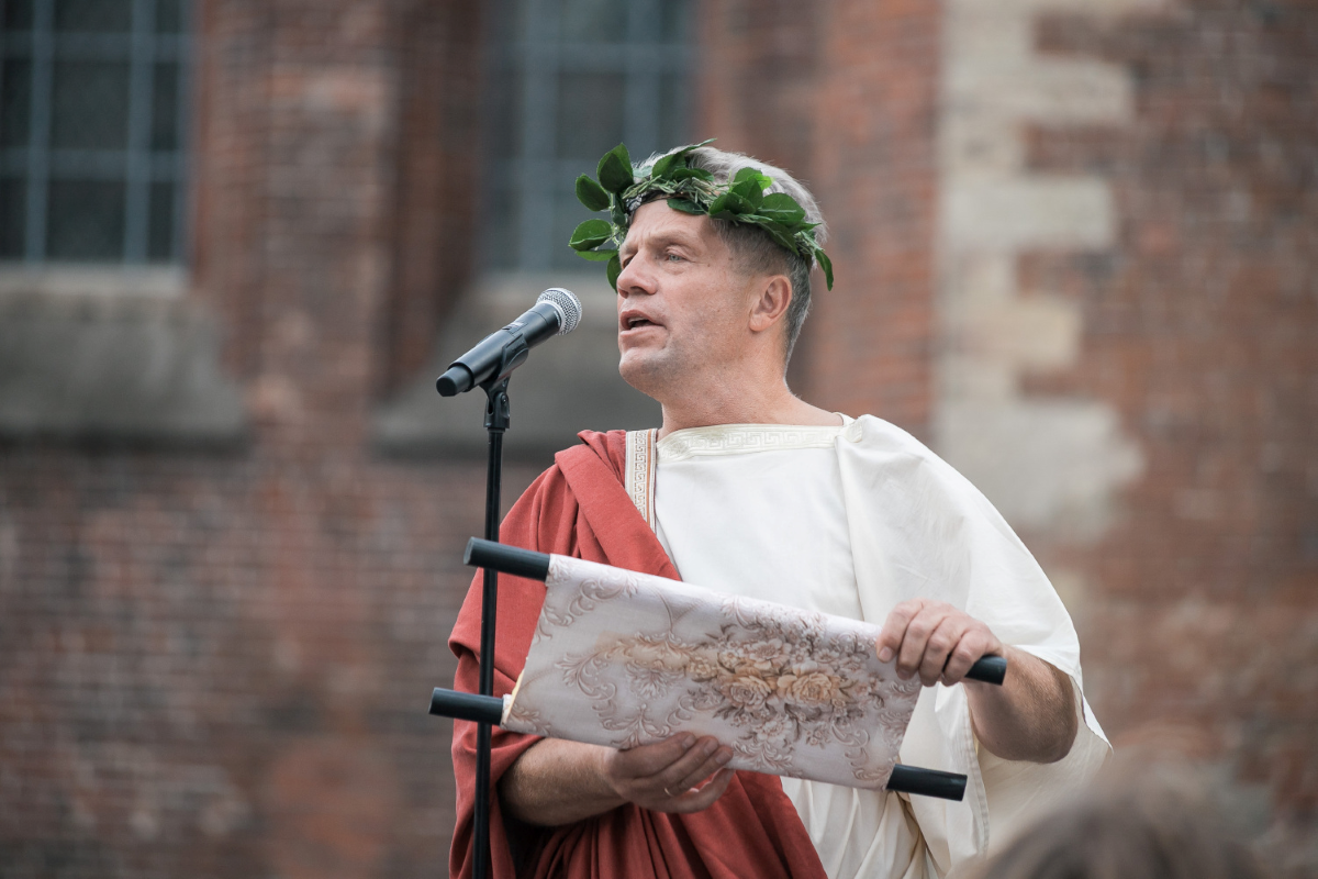 “Aristoteļa” tēlā tērpts runātājs uzrunā Latvijas Universitātes jaunos studentus pasākumā “Aristotelis 2026”.