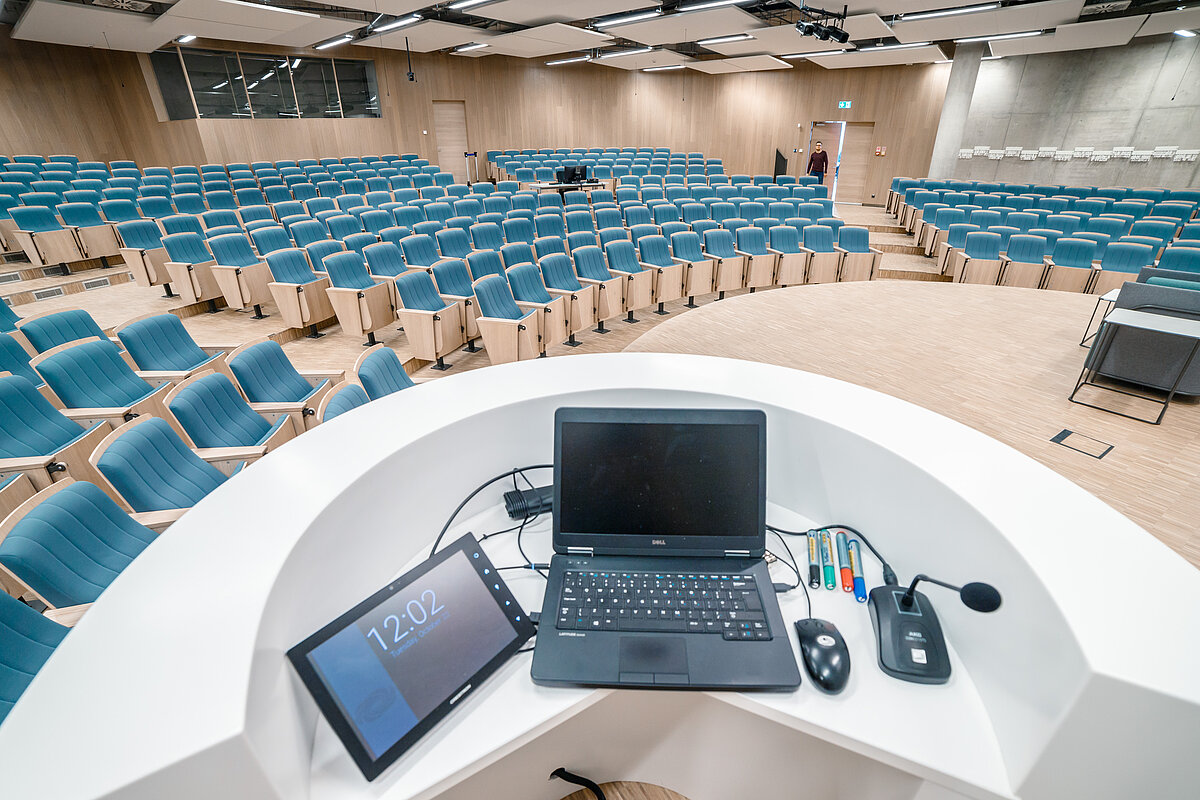 LU auditorijas lektora darba vieta ar portatīvo datoru, planšeti un mikrofonu vadības ierīcēm