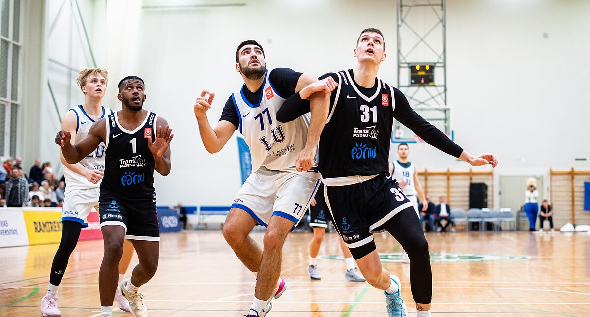 Basketbola spēles mirklis: četri spēlētāji cīnās zem groza