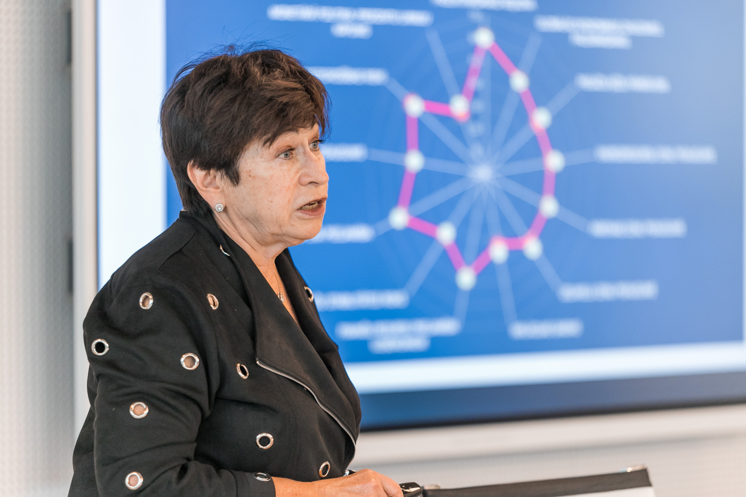 Inna Šteinbuka, fonā prezentācija, kurā redzamas datu līknes