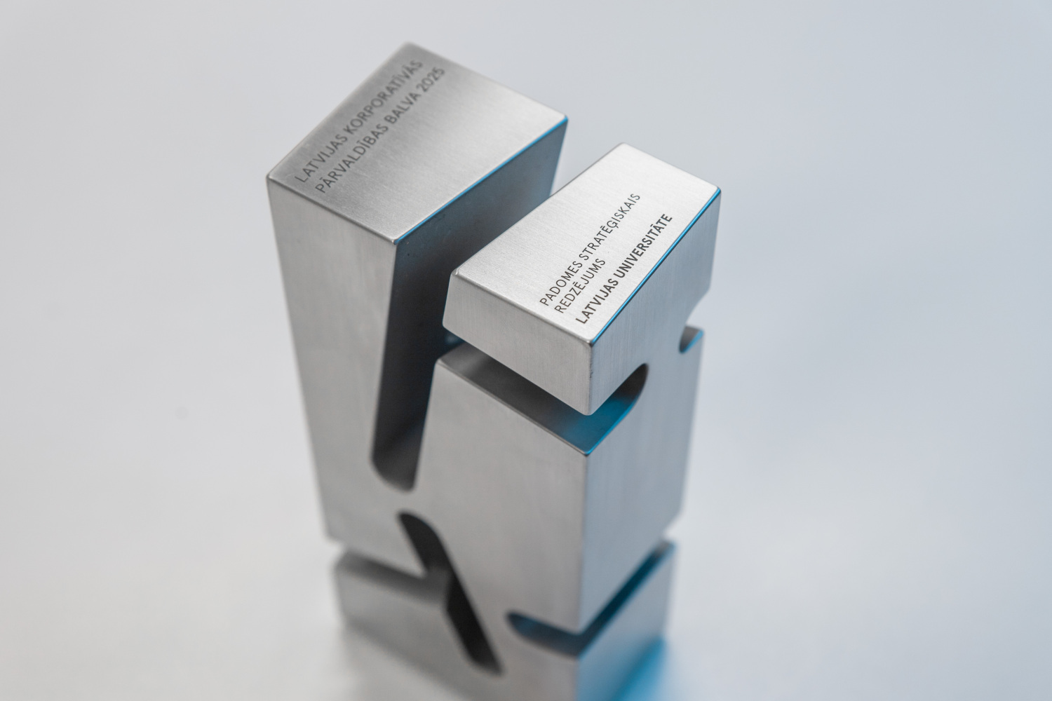 Uz balta pjedestāla stāv trīs sudrabaini metāla balvas uz zaļa fona