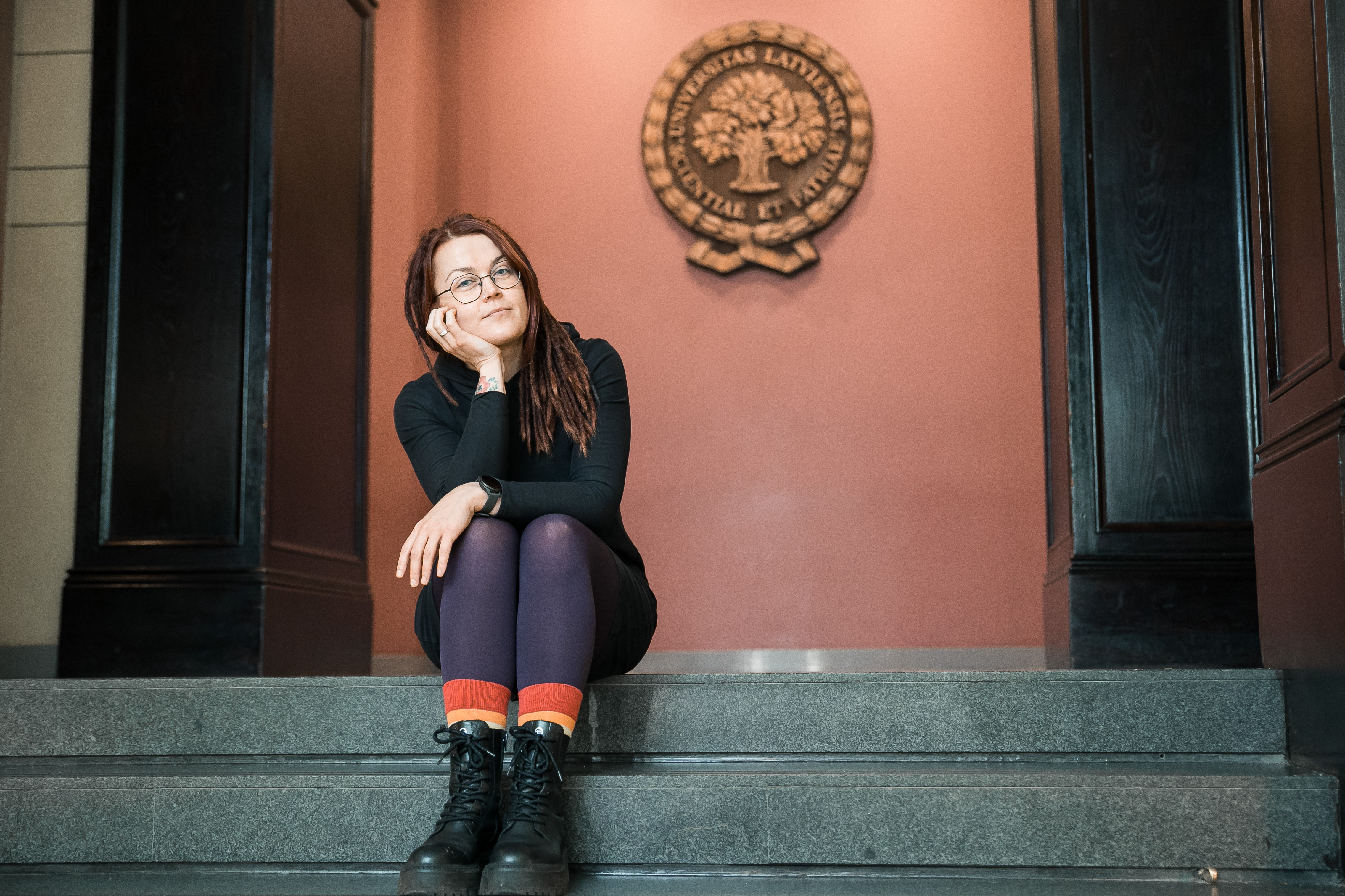 Velga Polinska Latvijas Universitātē uz kāpnēm, fonā LU ģerbonis