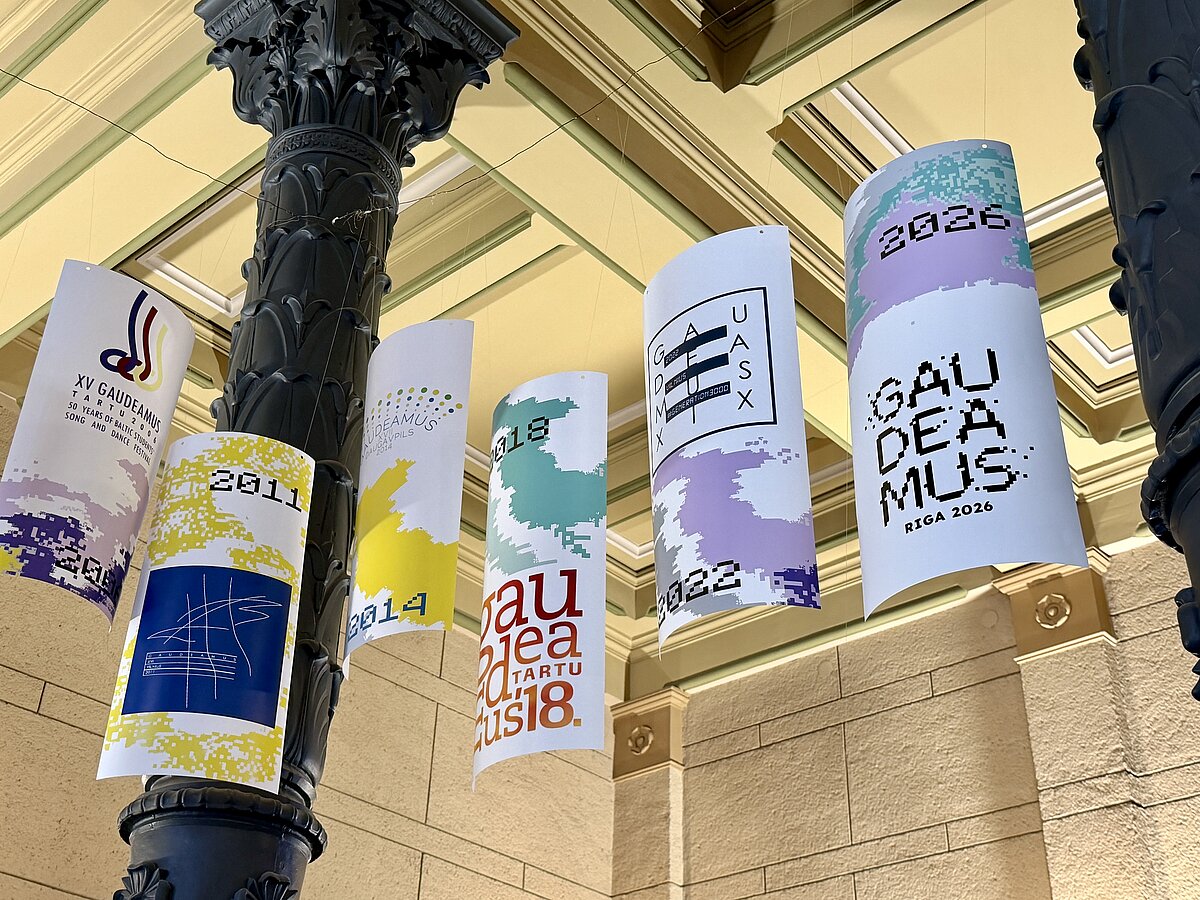 No griestiem piekārti vairāki vertikāli baneri ar dažādu gadu akadēmiskā mākslas festivāla “Gaudeamus” logotipiem. 