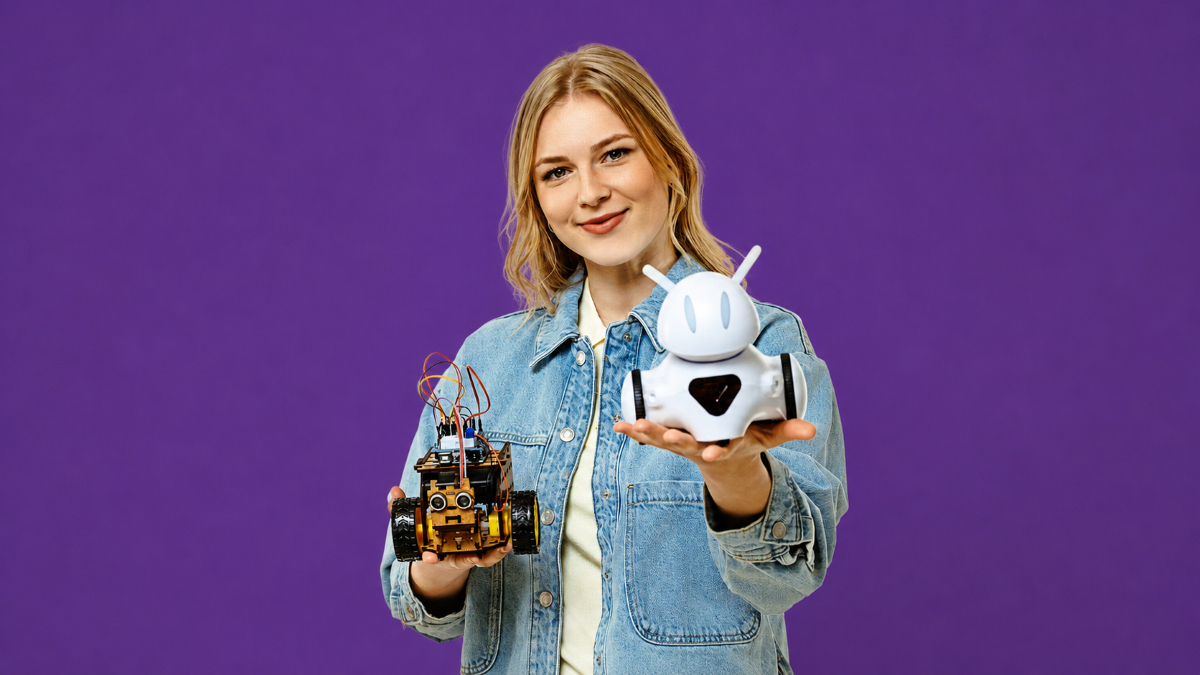 Studente džinsa jakā tur rokās divus robotus uz violeta fona.