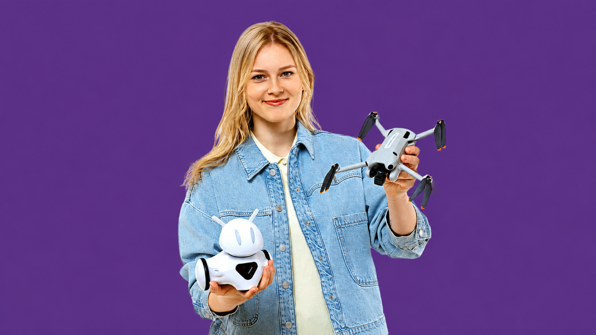 Persona džinsa jakā tur dronu un robotu uz violeta fona.