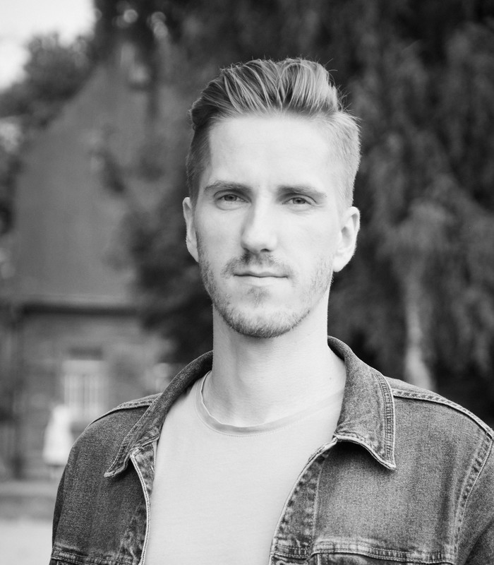 Gata Ezerkalna melnbaltais portretfoto džinsa jakā, fonā ēka un koki.