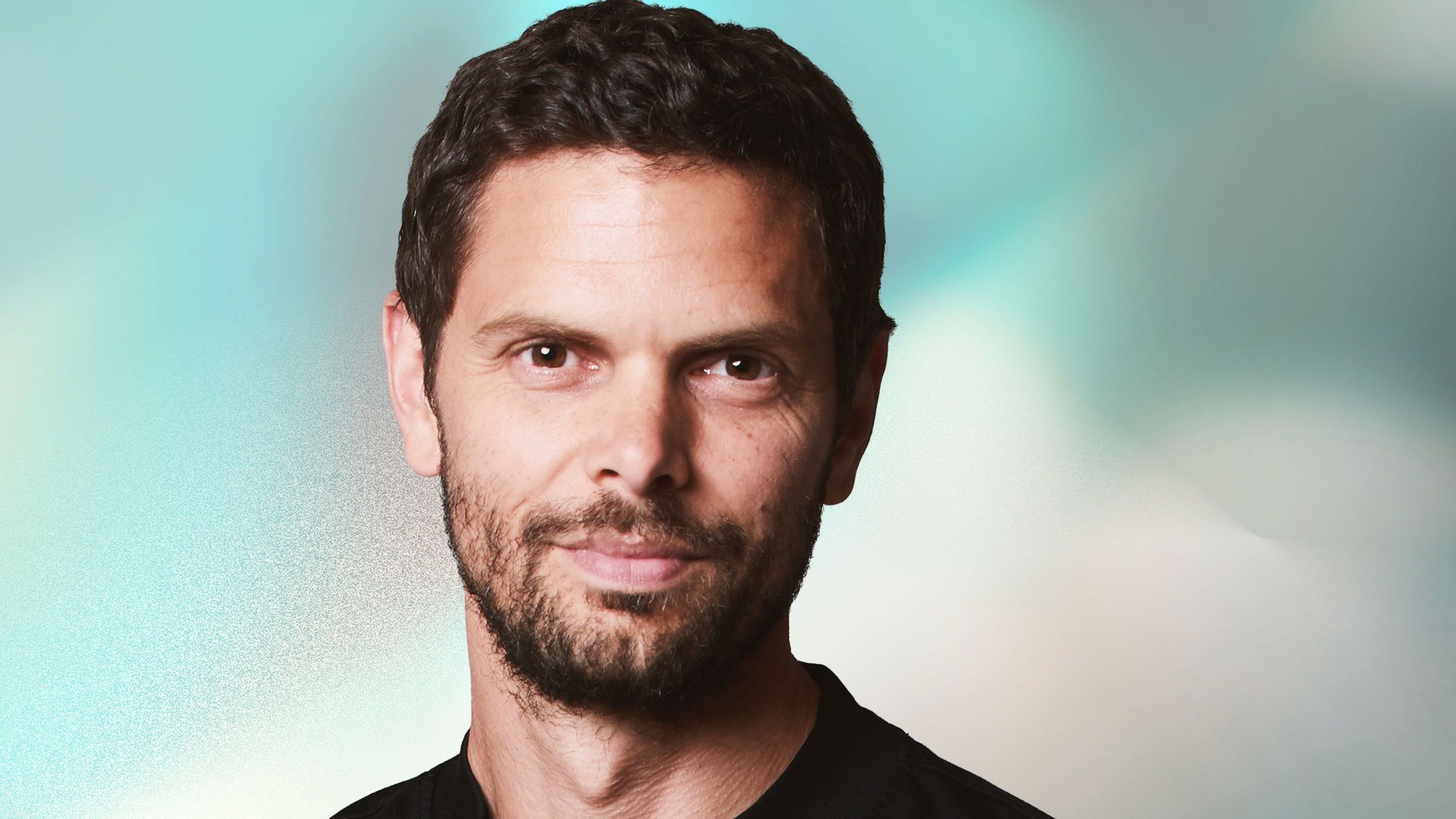 Peter Sarlin in a black t-shirt with a beard, against a blurred teal and white background.