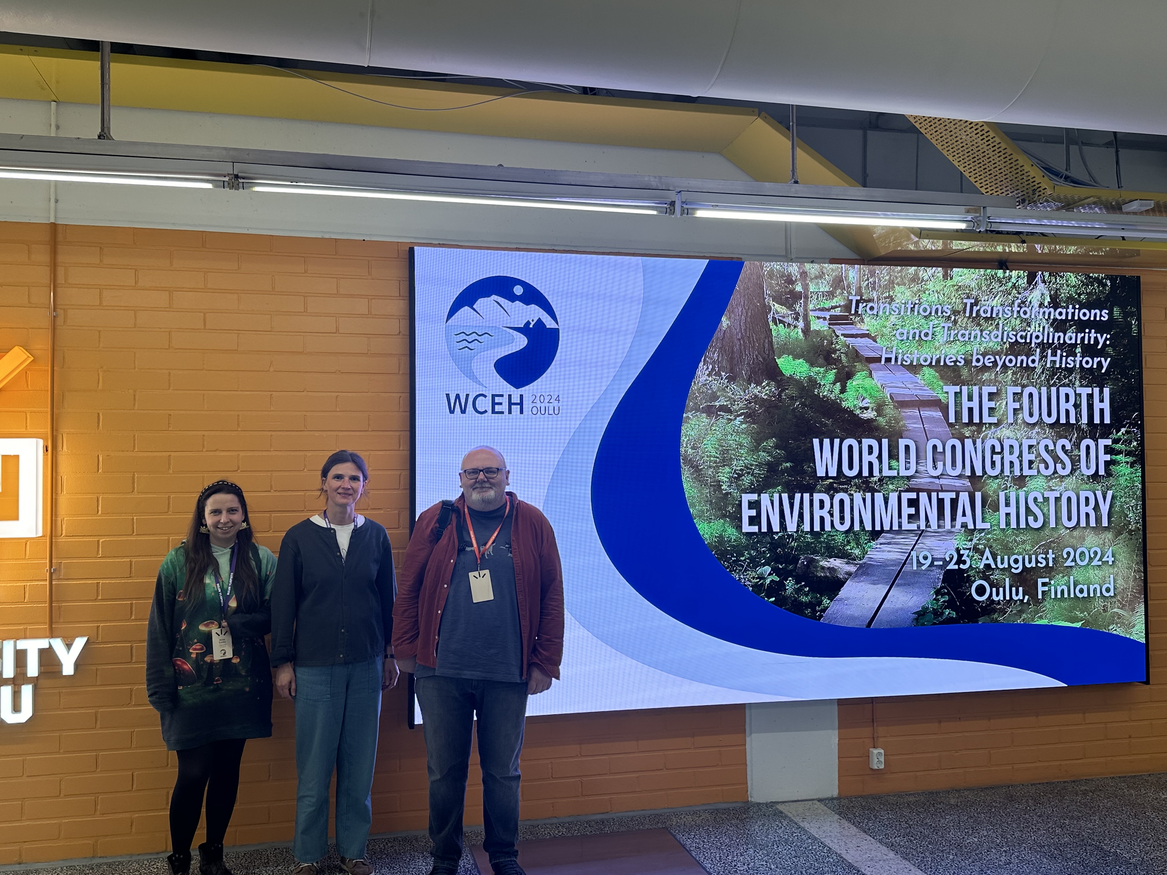 Attēla labajā malā ekrāns ar virsrakstu "Transitions, Transformations and Transdisciplinarity: Histories beyond History. Fourth World Congress of Environmental History. 19-23 August. Oulu, Finland". Kreisajā malā projekta dalībnieki (no kreisās): Anne Sauka, Anita Zariņa un Artis Svece.