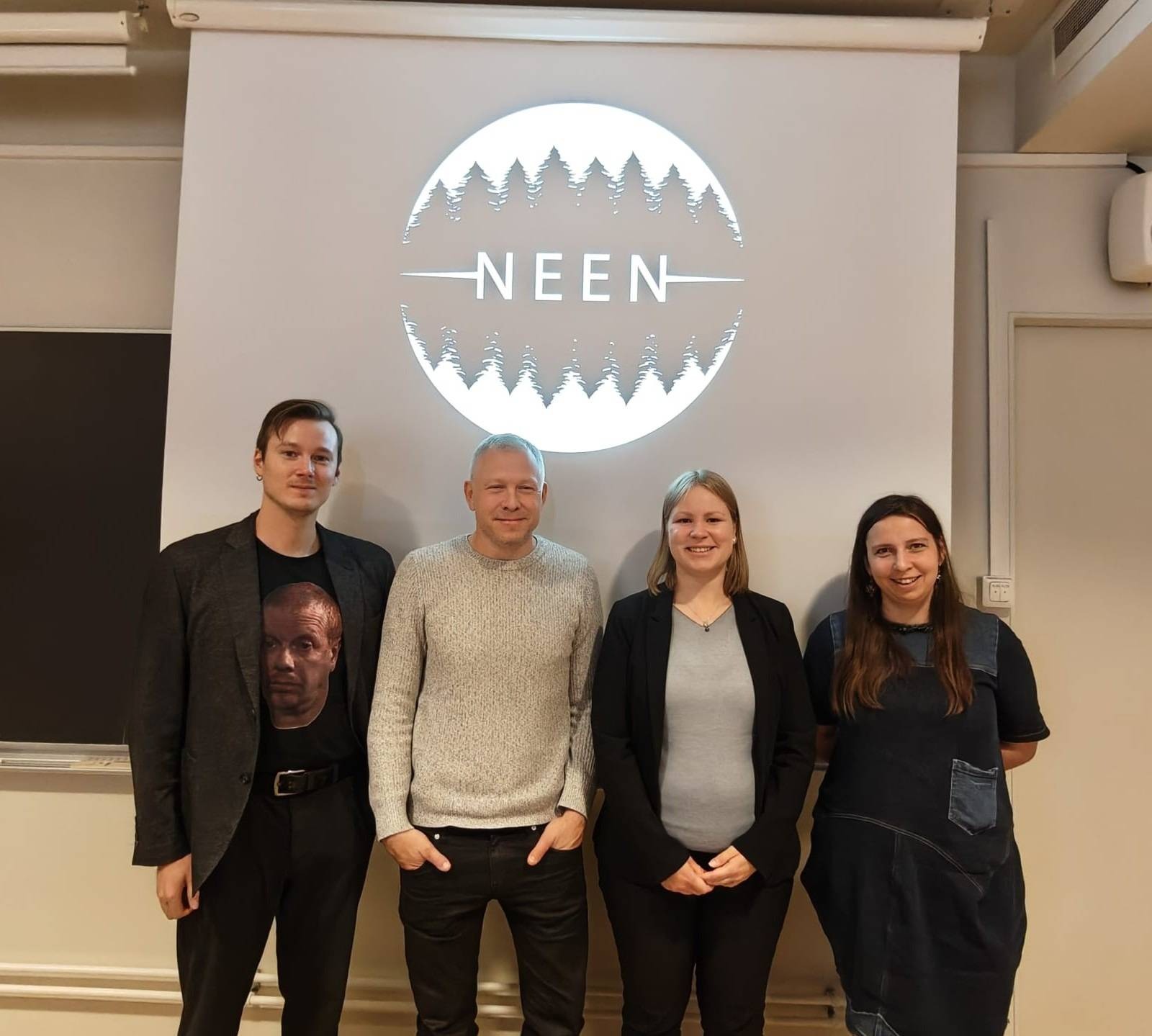 The photo shows four researchers with a presentation screen displaying the Nordic Environmental Ethics Network logo in the background. The first on the left is project researcher Anne Sauka.